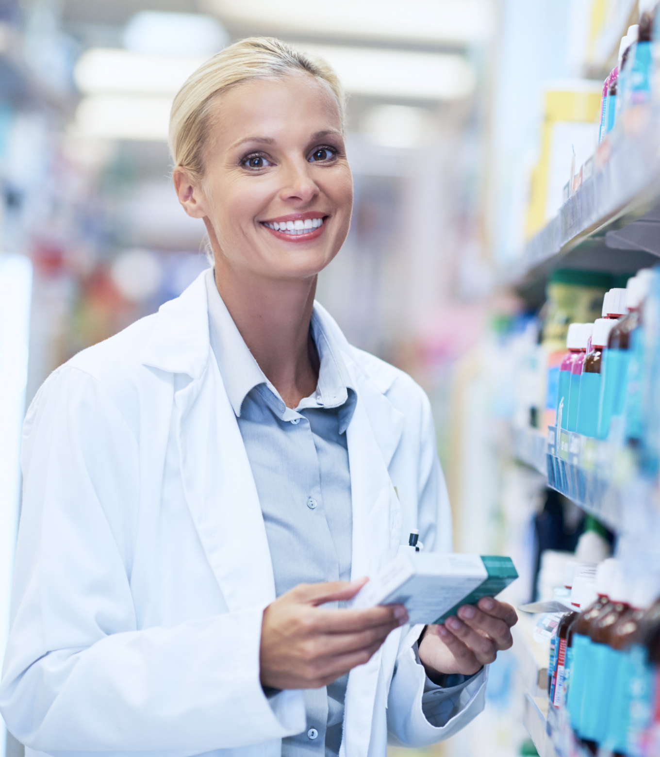 A woman in a white lab coat stands in a pharmacy aisle, surrounded by shelves of medicine and healthcare products.